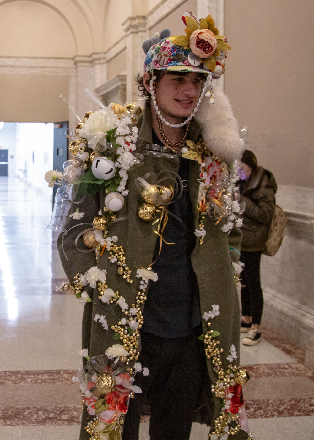 The "Sonitus Strepitus" features ornate embellishments on the shoulders, arranged in a dramatic diagonal perspective to enhance visual impact. The interplay of gold, red, and white hues highlights the military green, adding a distinctive and sophisticated elegance to the ensemble.